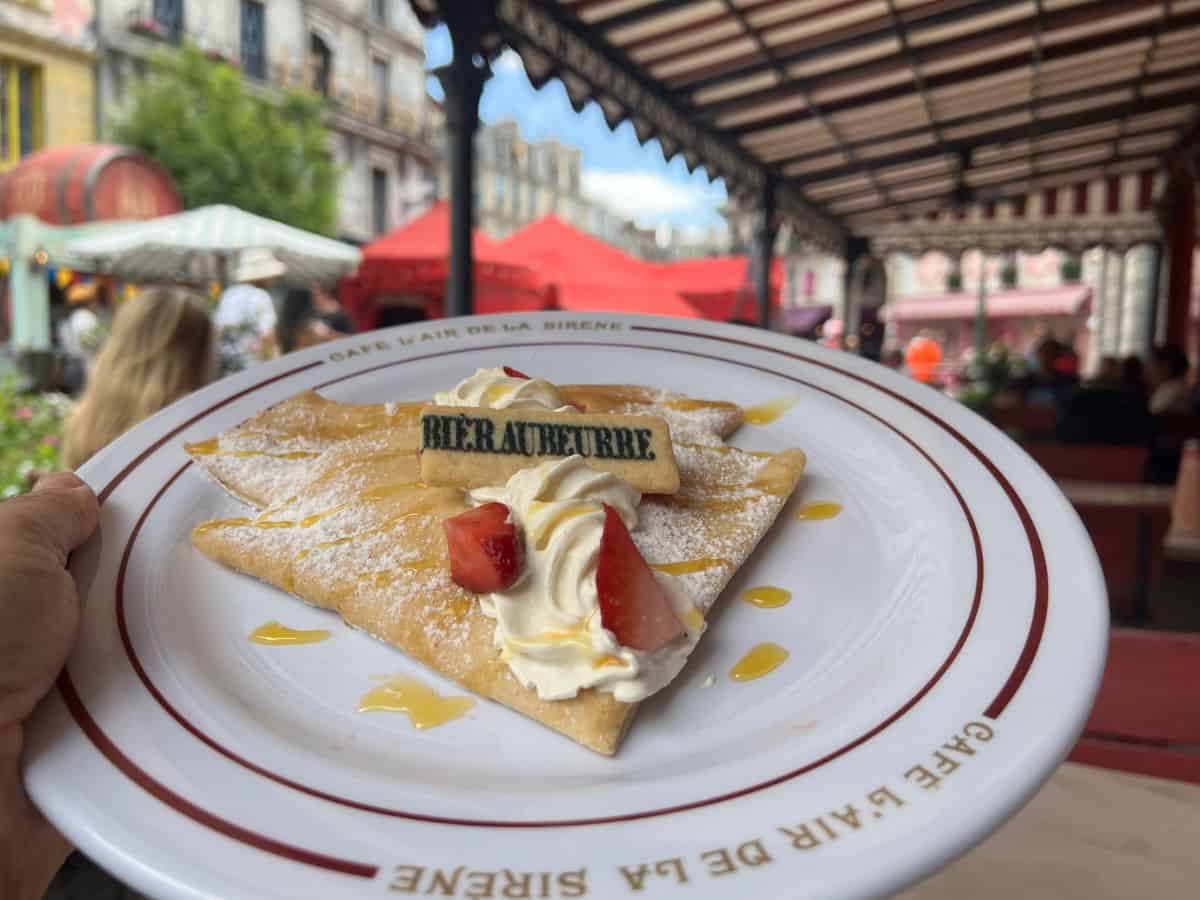 A hand holds up a plate of butterbeer crepes at the Ministry of Magic world in Epic Universe.