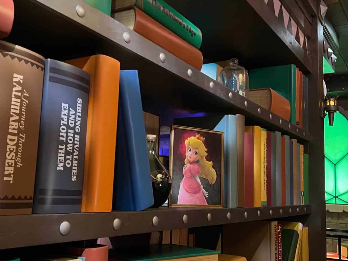 A picture of Princess Peach sits on a shelf between books in the ride queue of Mario Kart: Bowser's Challenge, Epic Universe.