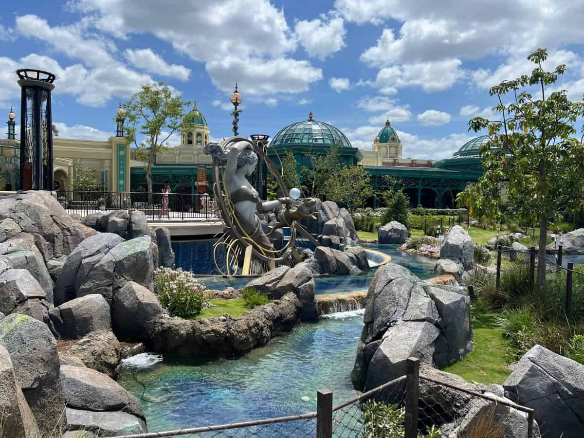 A statue of Luna rises above a fountain pool with a solarium in the background.
