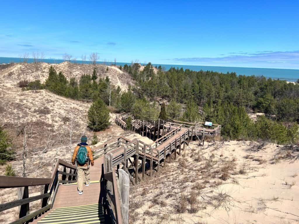 A man walks down a steep flight of stairs over sand dunes along the shores of Lake Michigan in Indiana Dunes National Park.
