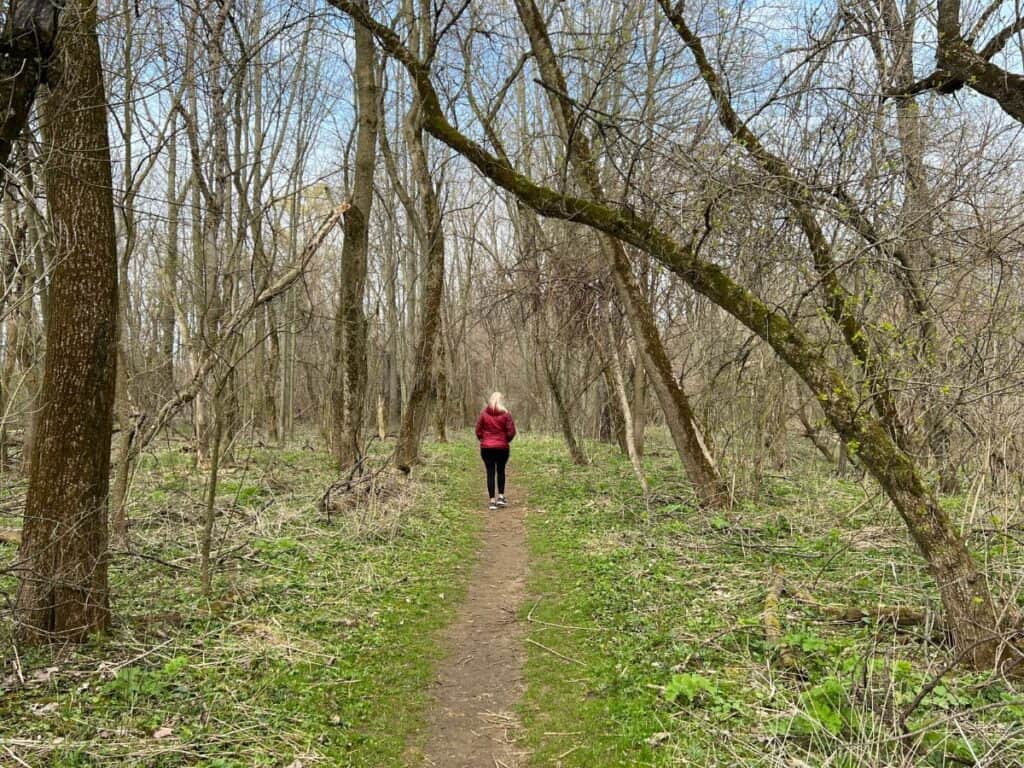 A woman walks along a forested trail - Heron Rookery is a great birding trail in Indiana Dunes National Park.