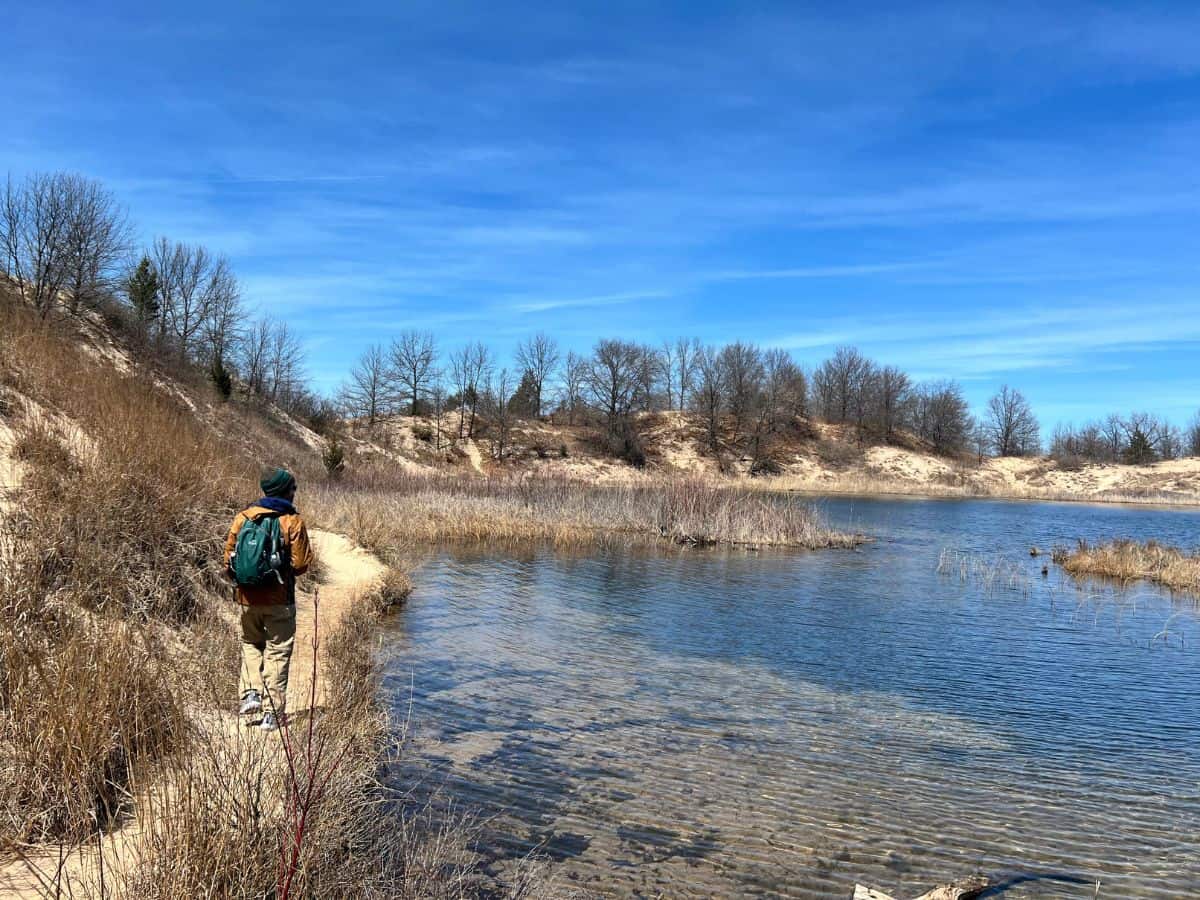 A man hikes a sandy trail along a lake