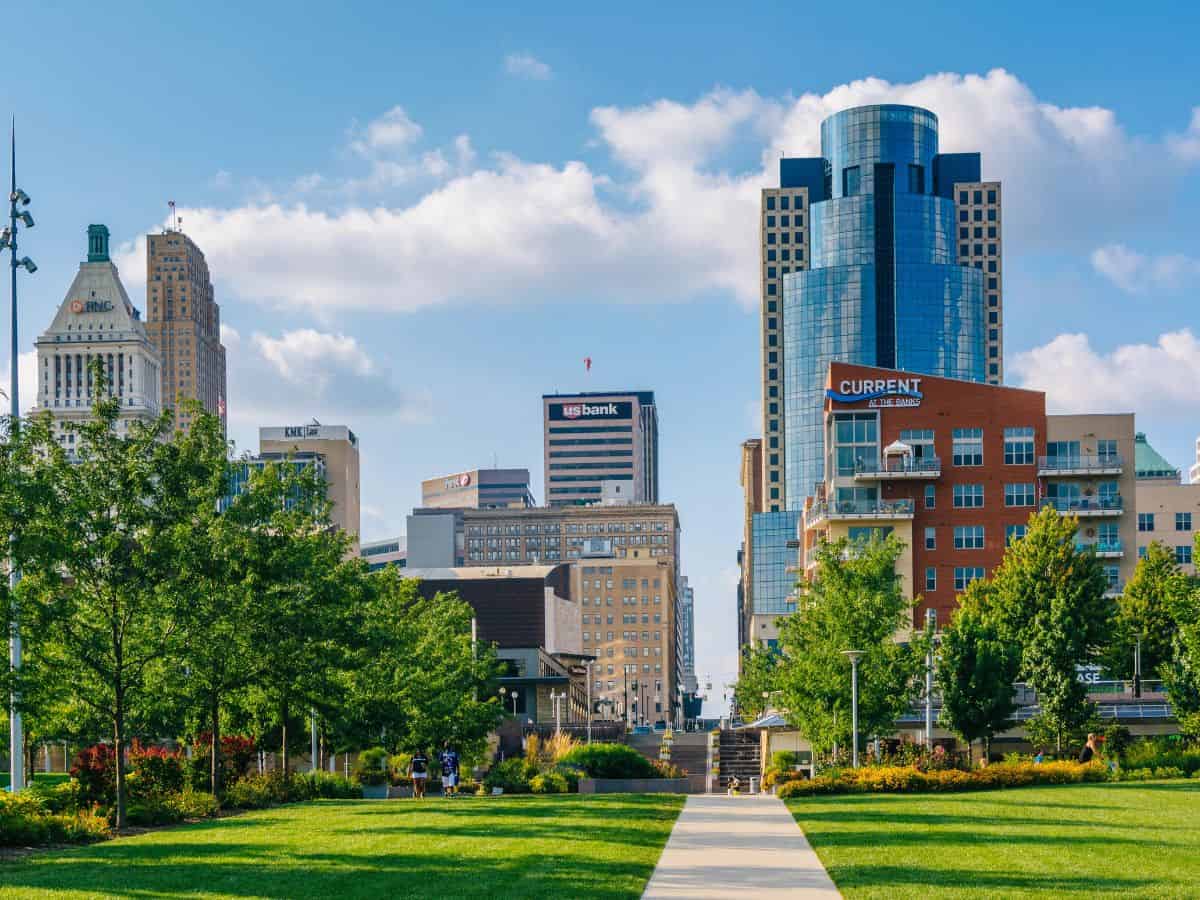 A sidewalk leads through a lawn of green grass ando toward city buildings