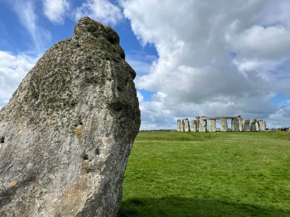 A moss covered stone in a field with Stonehenge in the background