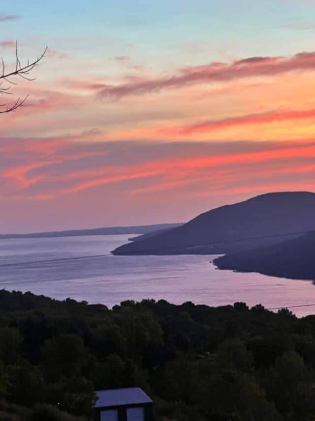 The early morning sky turns orange behind rolling hills along Canandaigua Lake in New York.