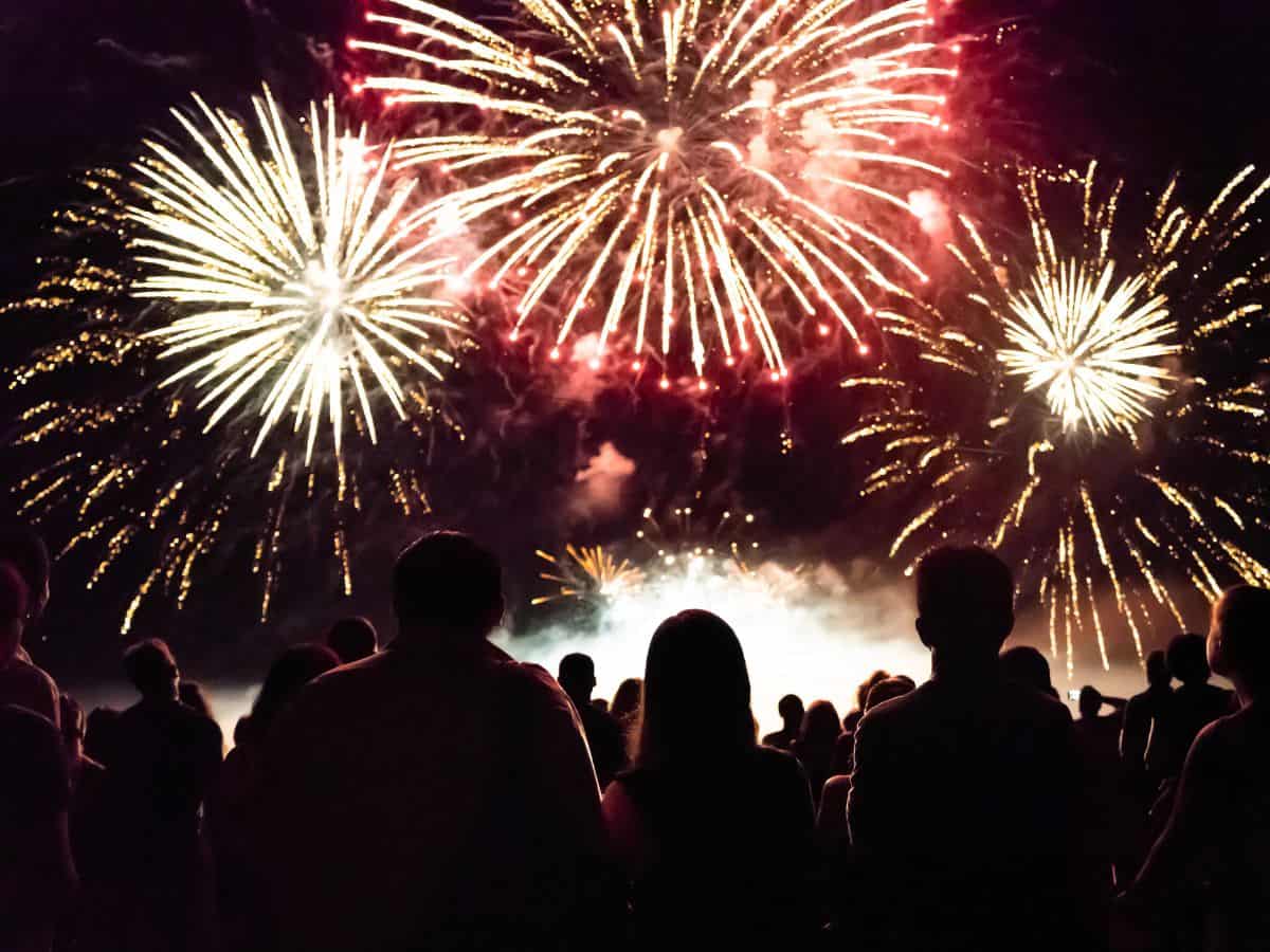 A crowd of people watch fireworks at night