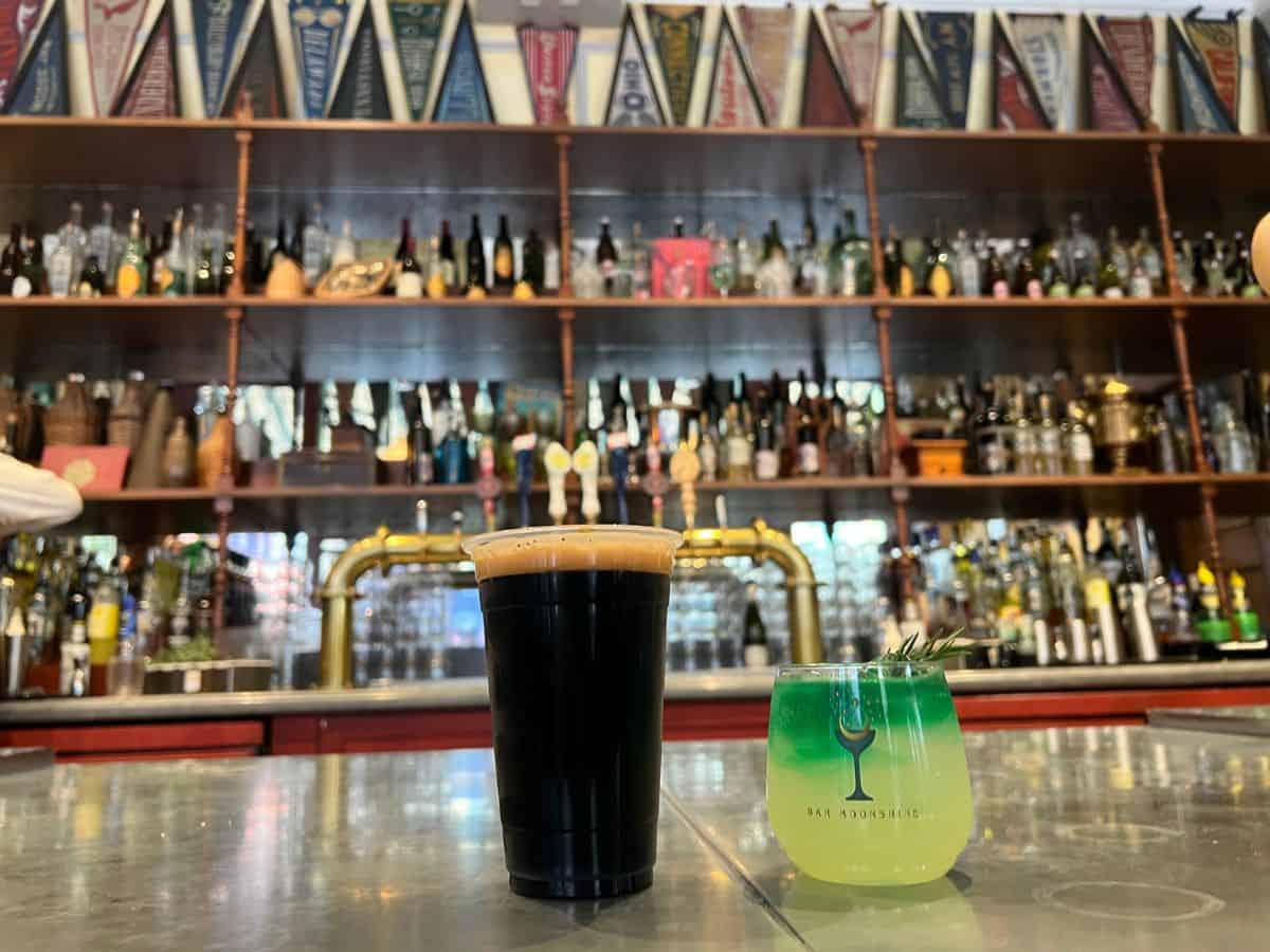A cup of dark beer and a cup with a colorful drink sit on a counter in an Epic Universe Harry Potter land bar.