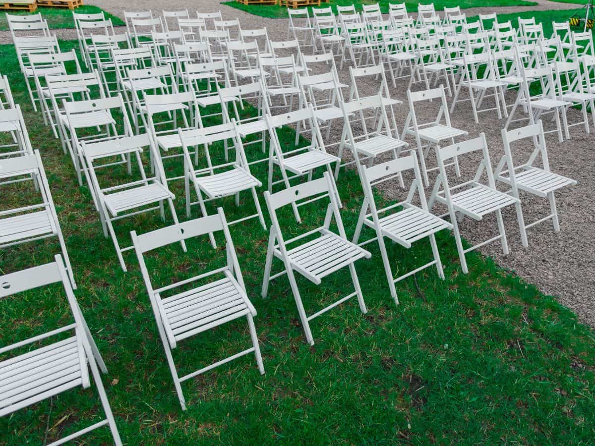 Rows of empty white chairs sit on a lawn.