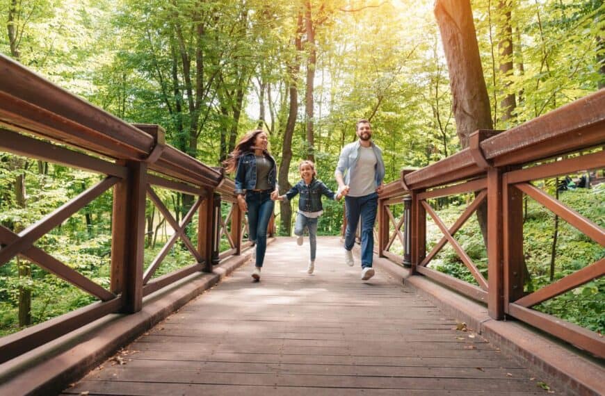 A husband, wife, and daughter run across a footbridge in the forest on their staycation.