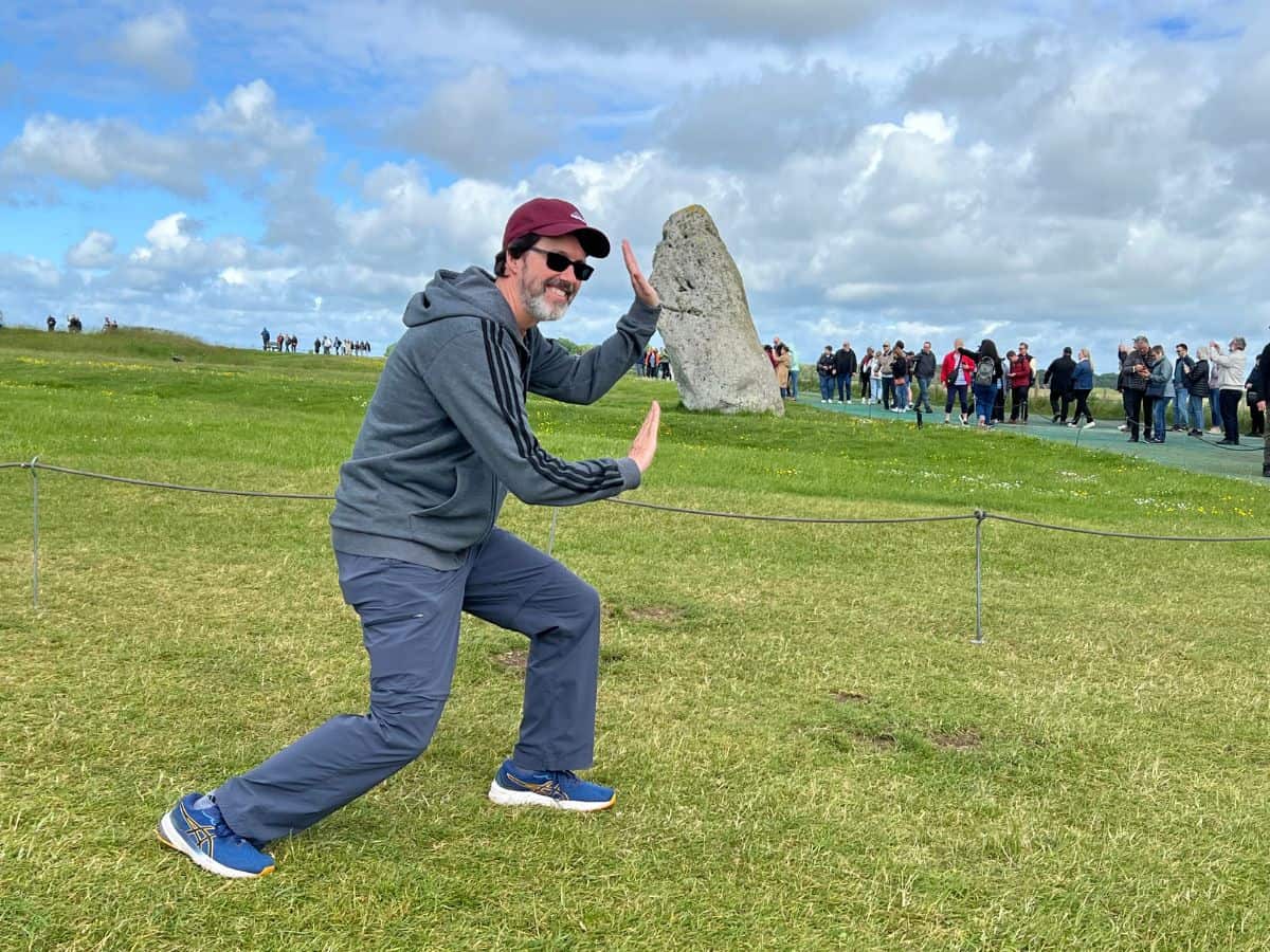 A man pretends to hold up a stone from falling at the Stonehenge site. Some view the photo spots as a pro of visiting Stonehenge, while others see it as a con of visiting Stonehenge.