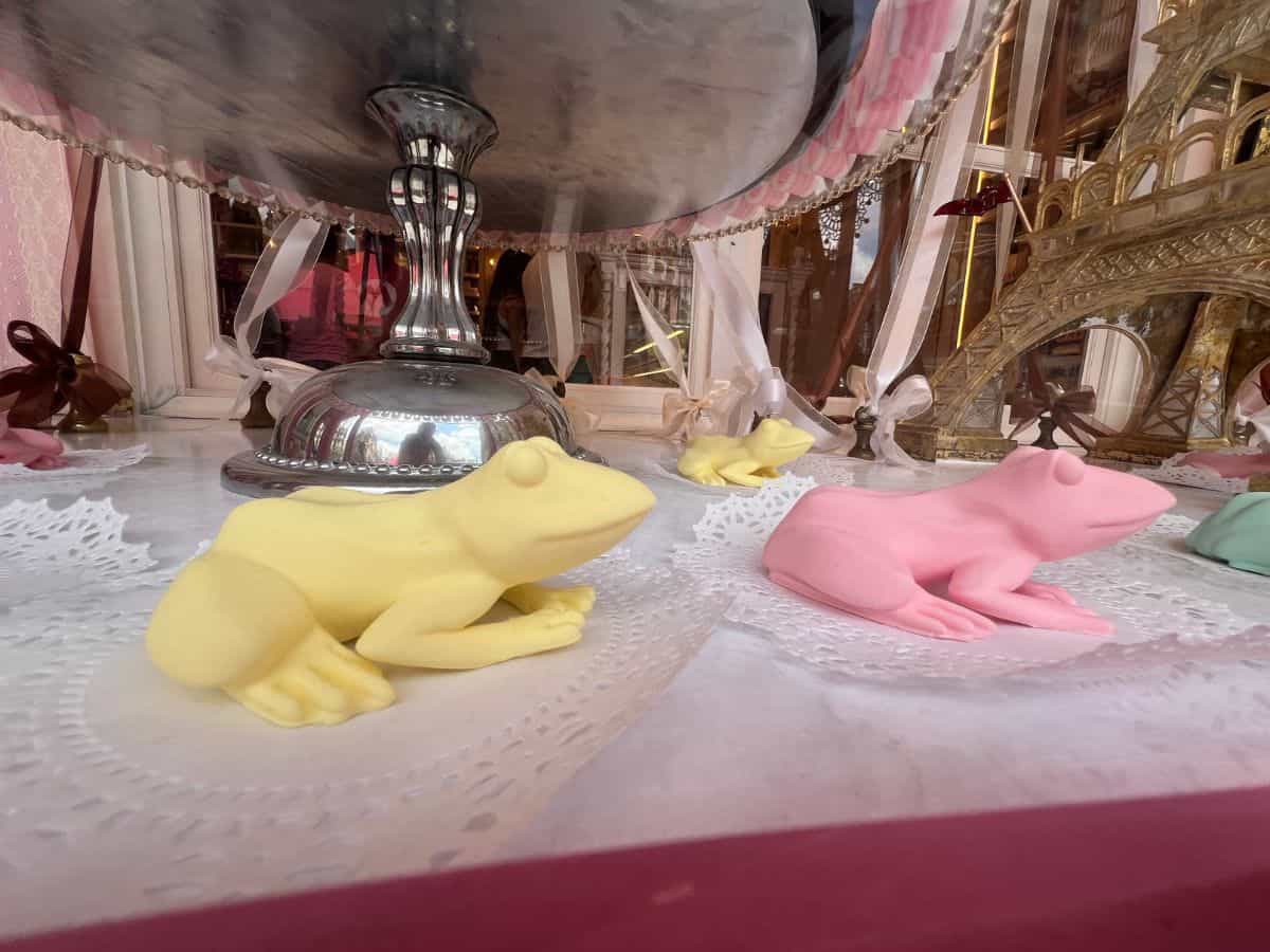 A yellow frog and a pink frog sit in a store display window in the Ministry of Magic at Epic Universe.