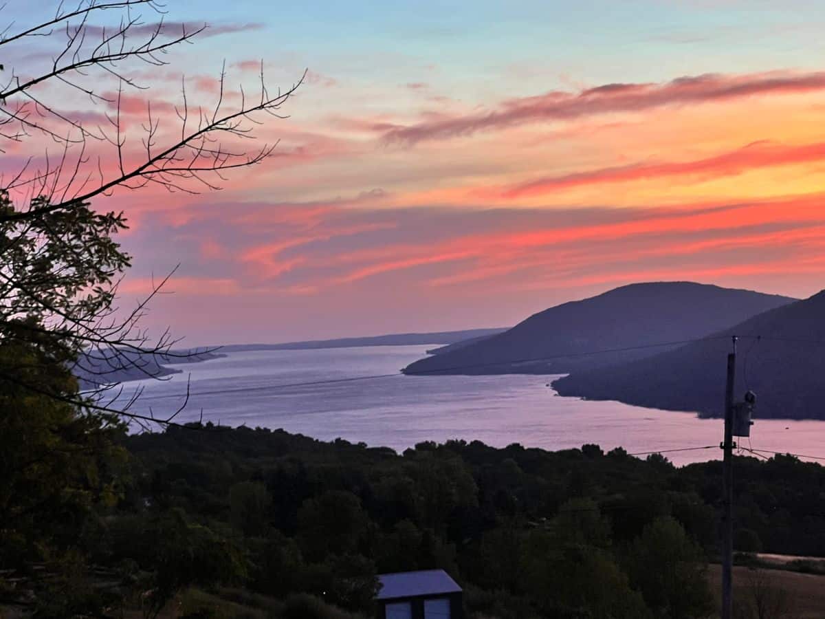 The early morning sky turns orange behind rolling hills along Canandaigua Lake in New York.