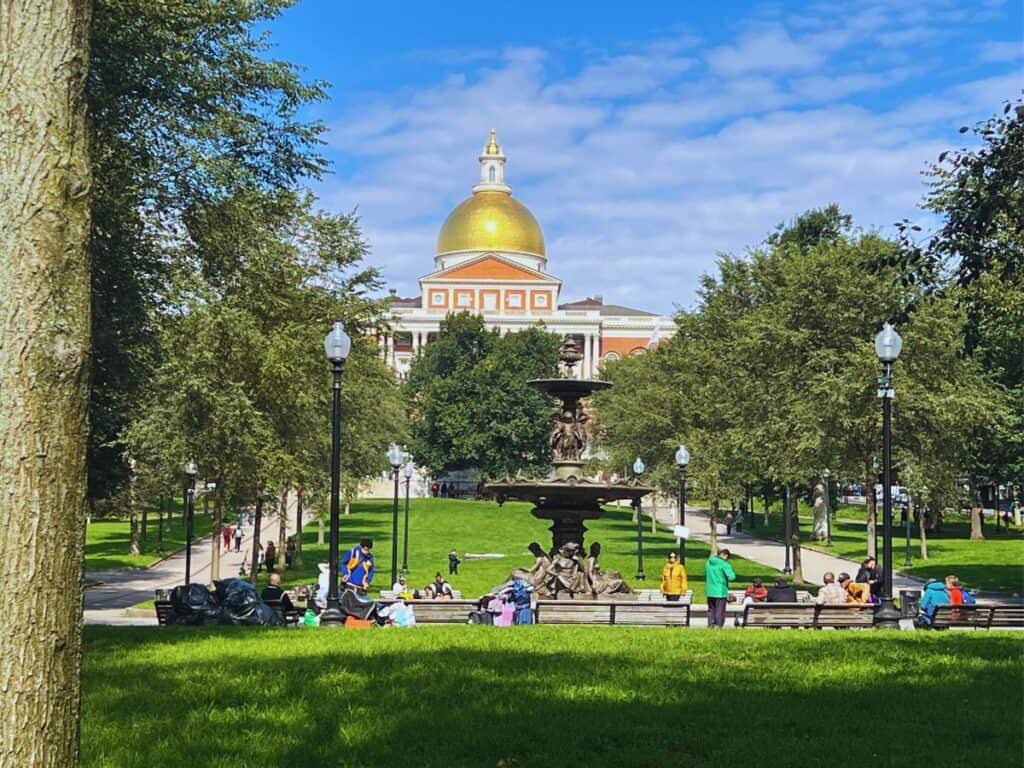 People sit on benches in a park near the Massachusetts State House