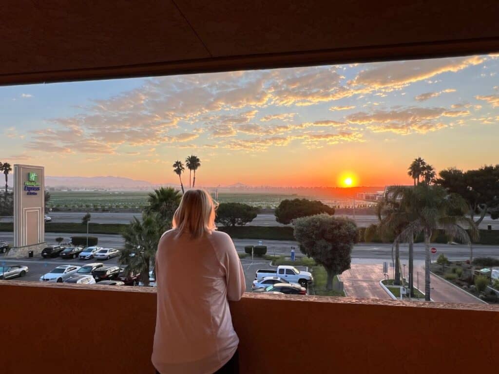 A woman watches sunrise just outside her hotel room in Ventura, CA.