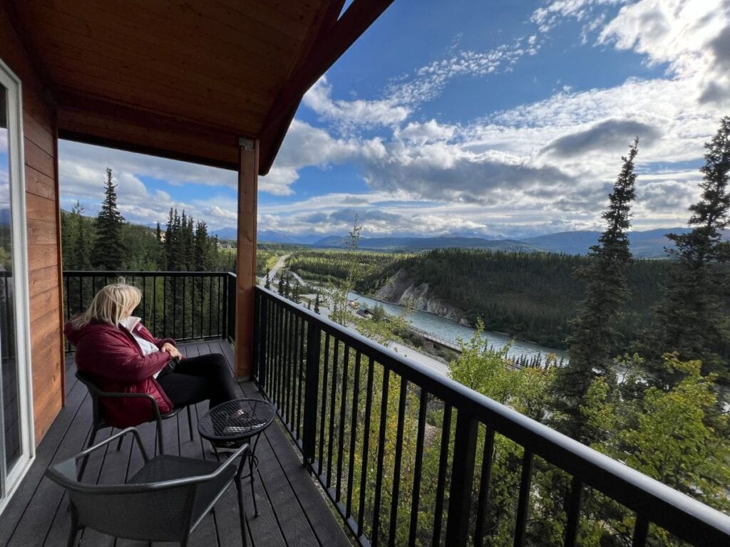 A woman sits on a balcony savoring a view of Denali National Park in the distance
