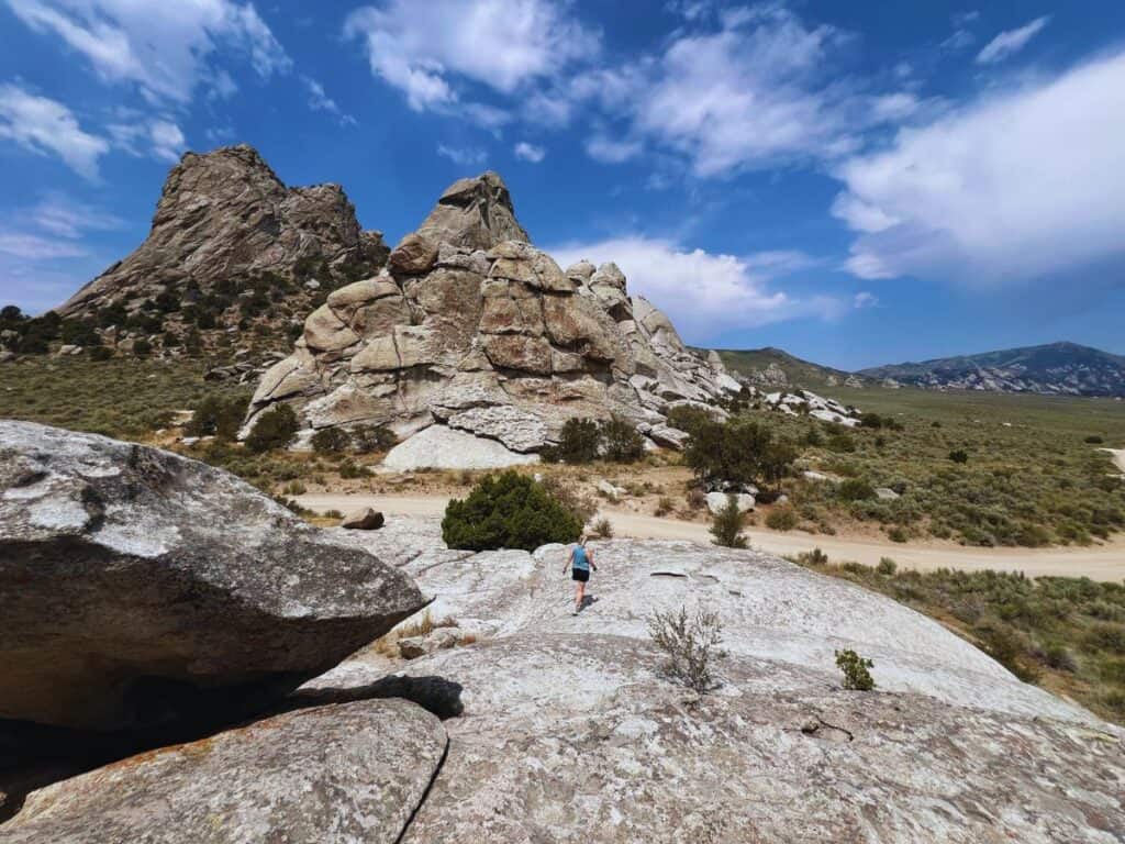 A woman walks down a giant monolith with more granite spires and monoliths in the background in City of Rocks National Reserve, Almo, ID
