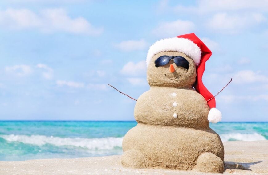 A sandy snowman represents Christmas in July travel - some locations celebrate the popular holiday in summer for a fun twist.