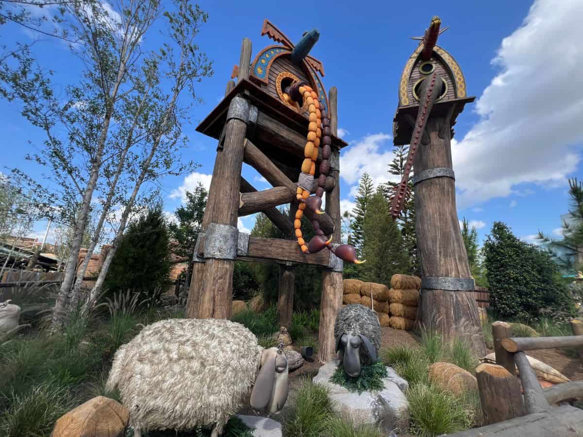 Sheep graze below dragon houses, where dragon tails dangle and swing below as the dragons nap