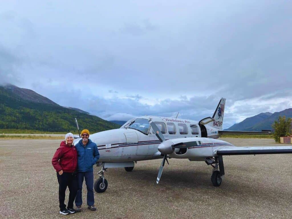 Scott McConkey and Julie McConkey of the Miles with McConkey Travel Blog stand in front of a small plane in Coldfoot, Alaska, above the Arctic Circle.