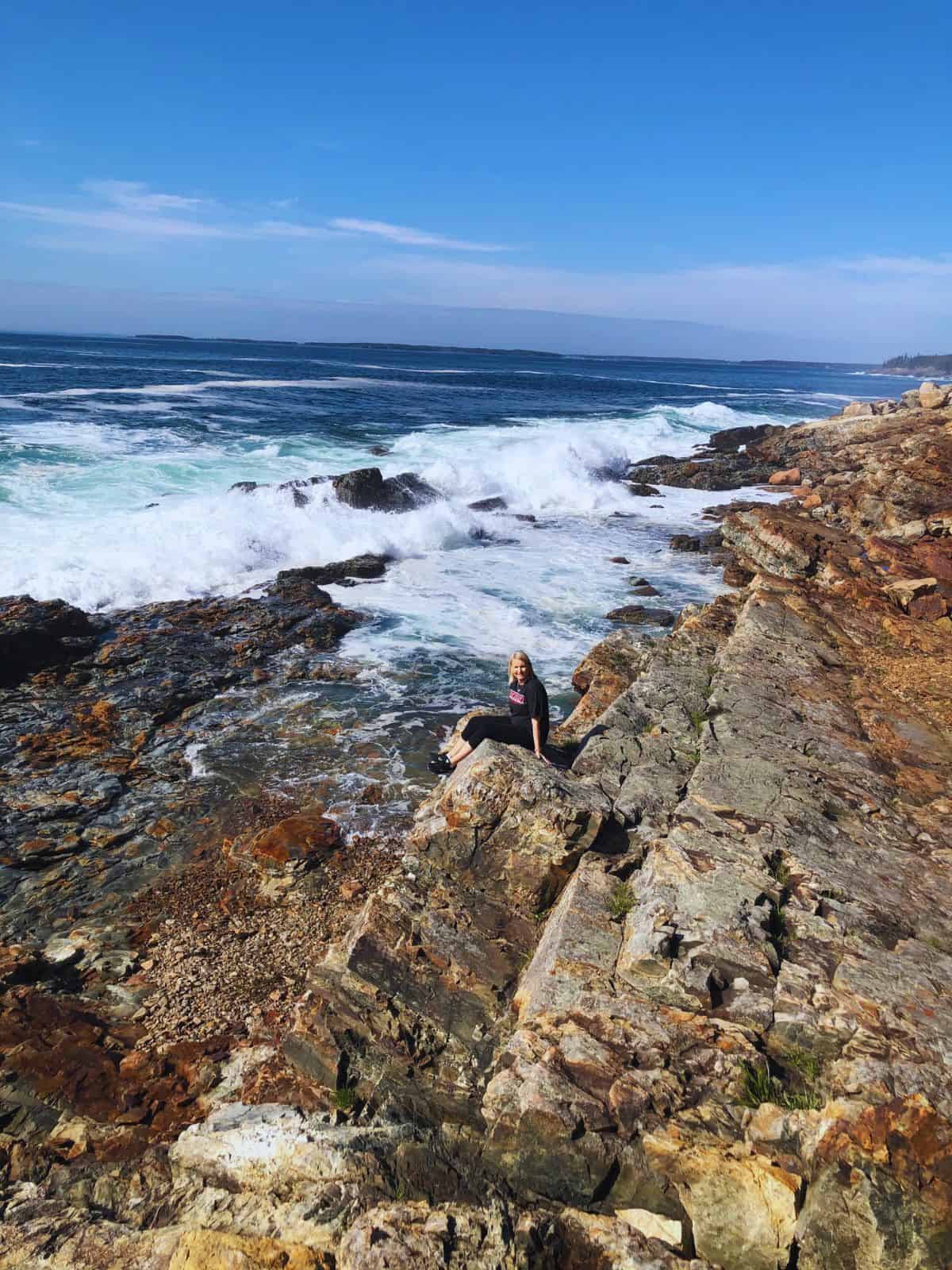 A woman enjoys the views of crashing surf along rocky shores - one of the best things to do in Acadia National Park, ME