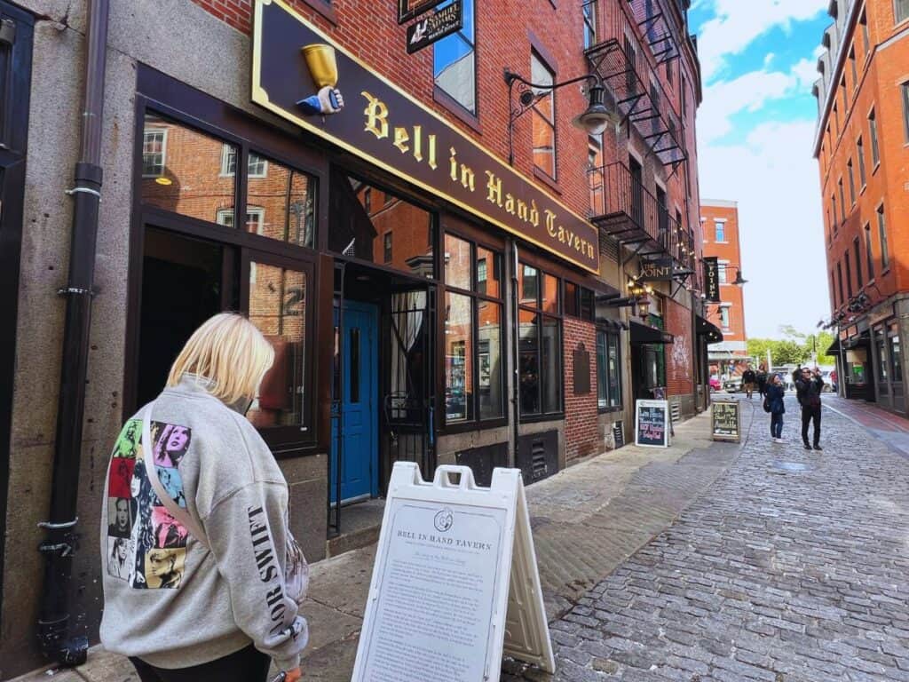 A woman pauses to read a sign outside the Bell in Hand Tavern - an excellent place for Freedom Trail food in Boston, MA