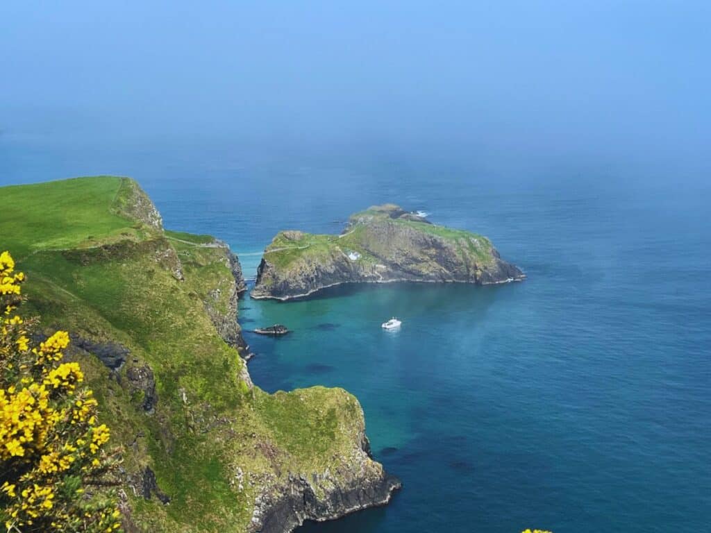 A rope bridge stretches from a green cliff below to a small island