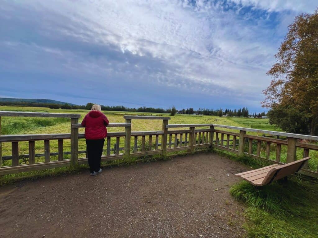 A woman leans agains a wooden rail and looks out across a vast field in Fairbanks, AK