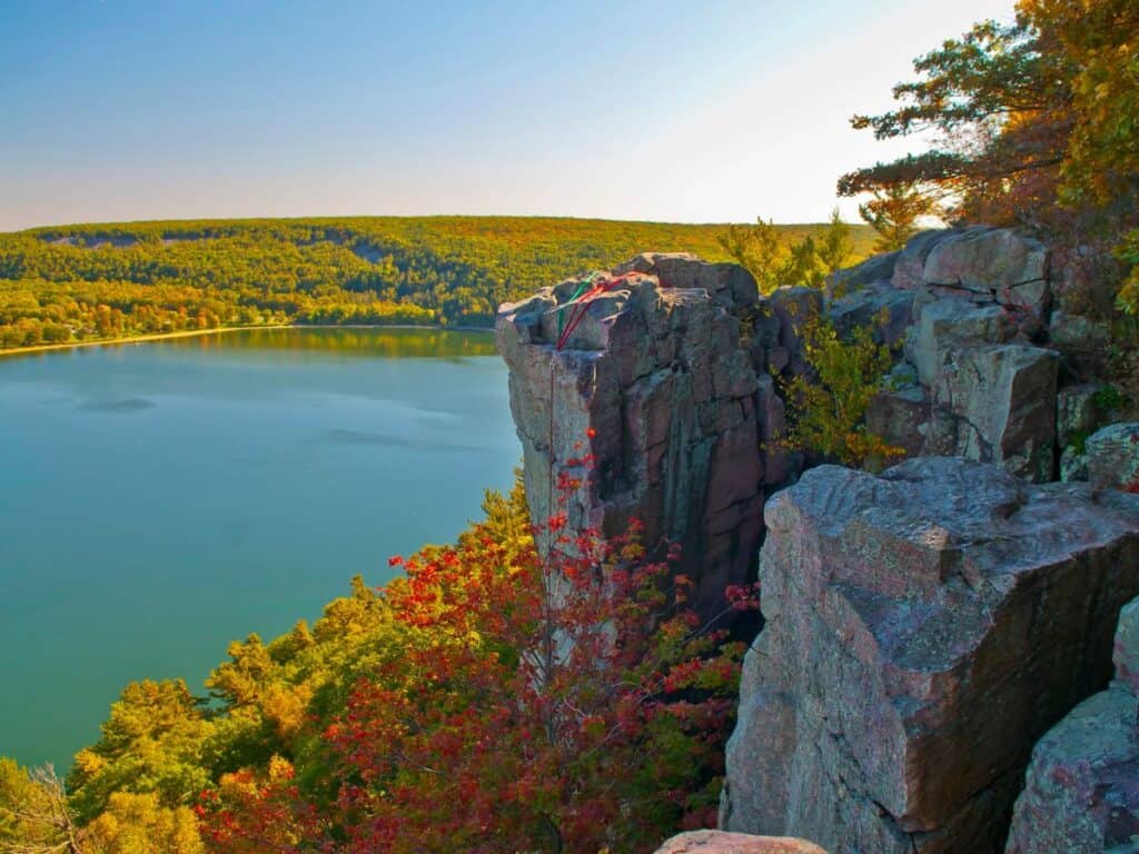 Rocky cliffs rise above a lake surrounded by trees starting to show fall foliage