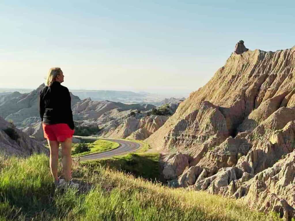 A woman looks at a road that winds downward through Badlands National Park, South Dakota