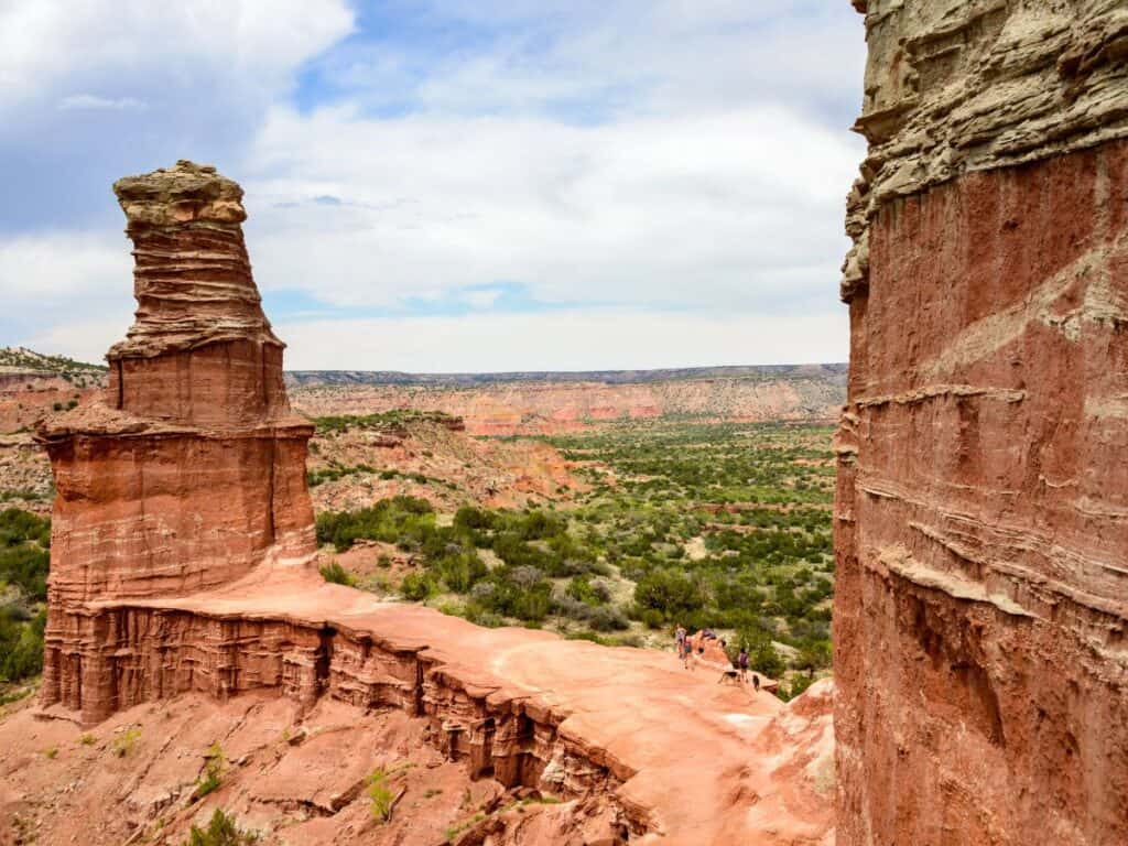 A towering rock formation that resembles a lighthouse stands out along a cliff of red rocks