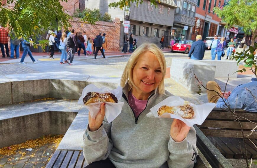 A woman smiles while holding up two cannoli just outside the Paul Revere House on the Freedom Trail