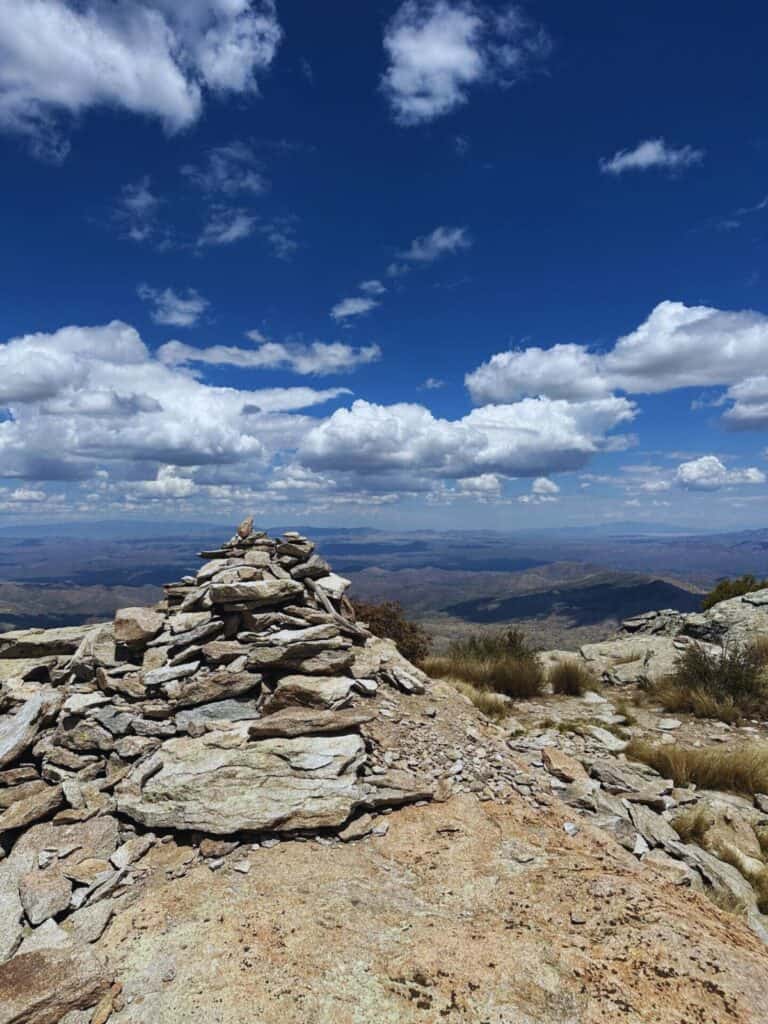 A mountain peak overlooks a sweeping valley below with blue skies and white puffy clouds