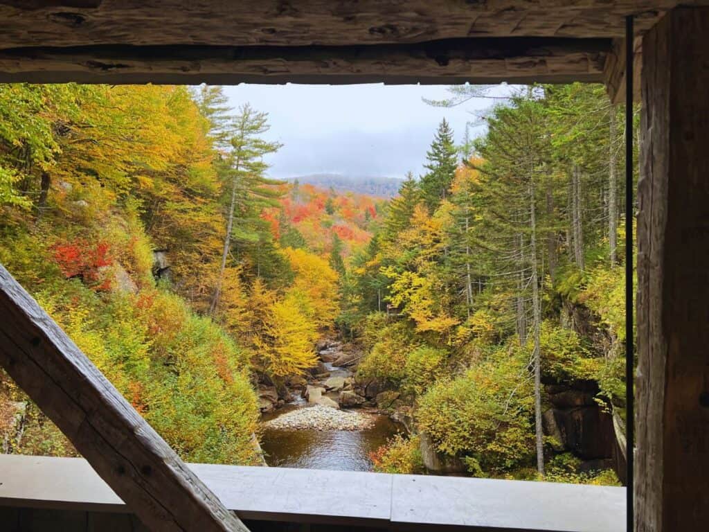 Fall foliage and a stream as seen through the window of a covered bridge on the Flume Gorge Trail
