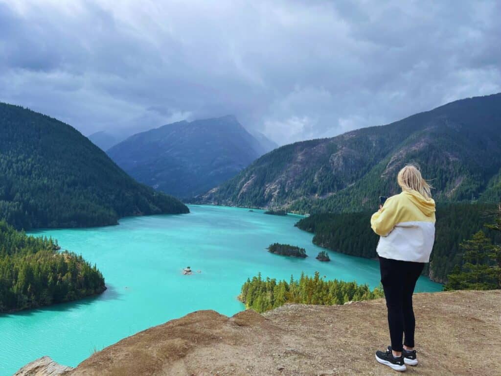 A woman takes a picture of Diablo Lake with her phone.
