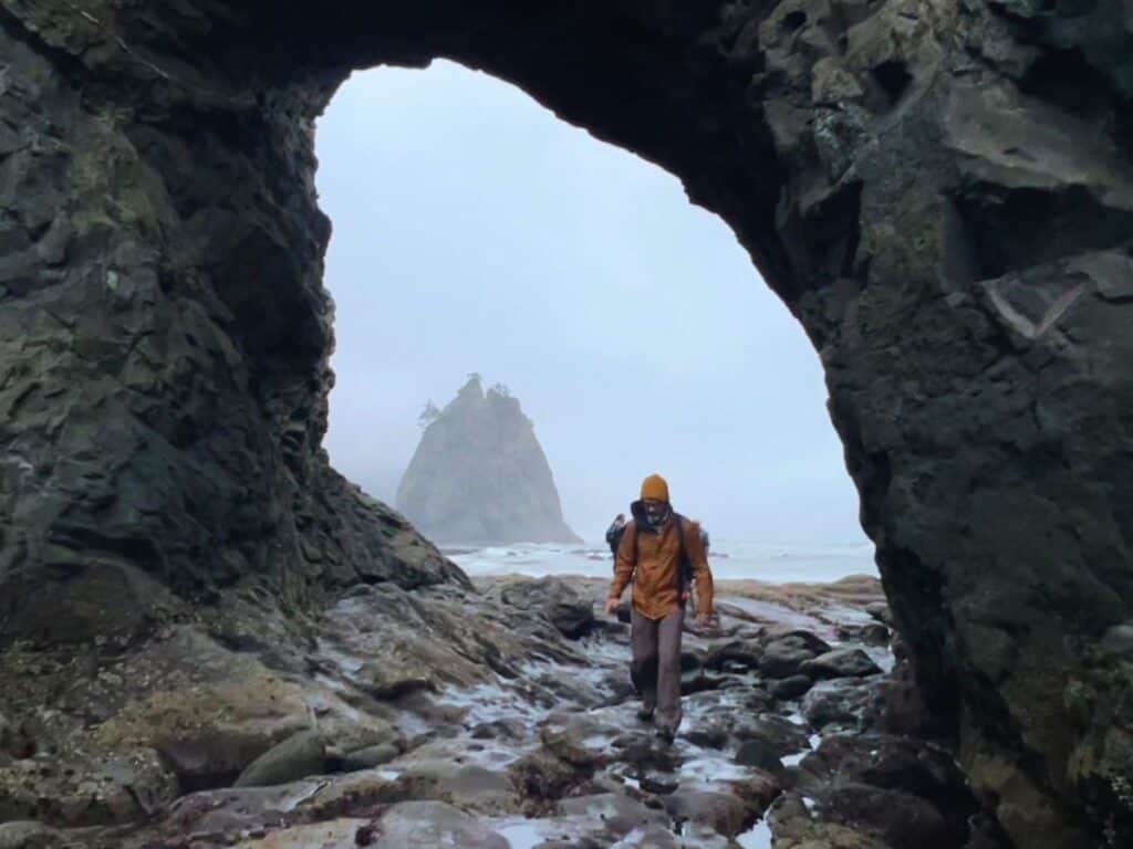A man walks through Hole in the Wall, Olympic National Park, Washington