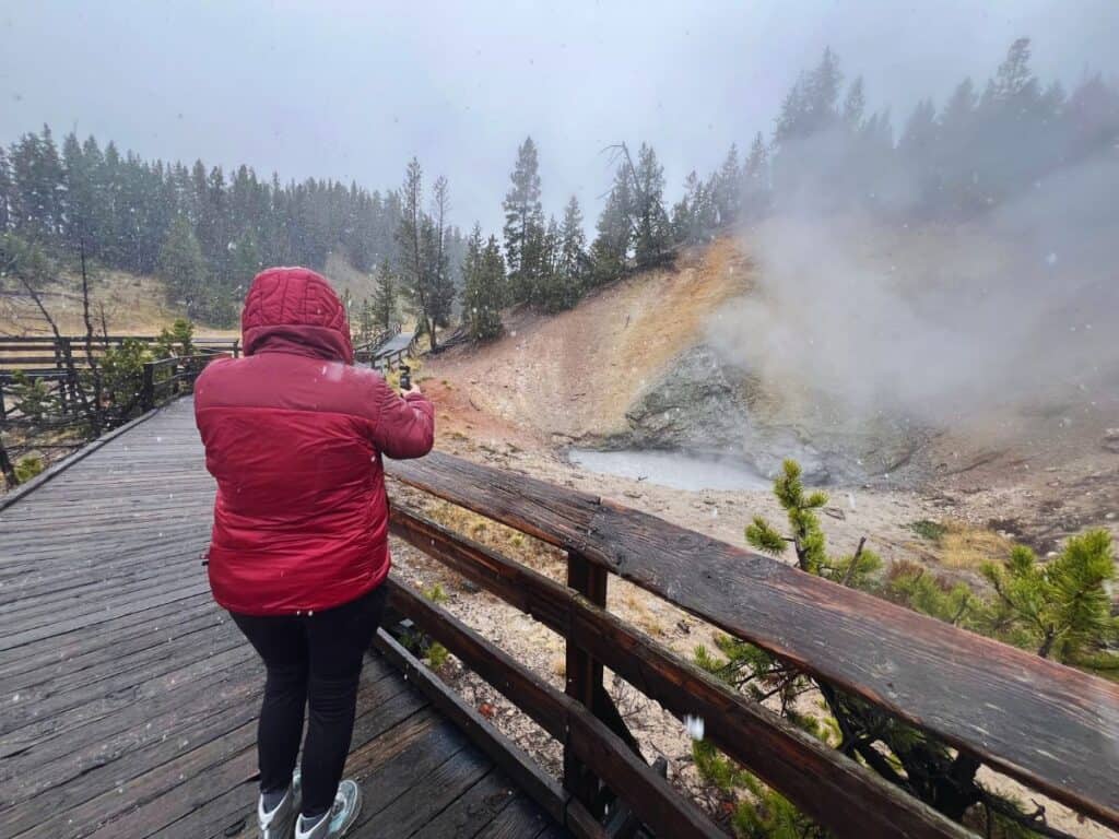 A woman takes video footage of Mud Volcano in Yellowstone National Park as a light snow falls.