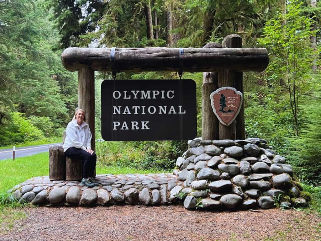 A woman sits by the Olympic National Park sign