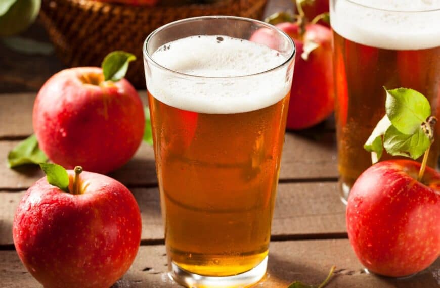 Apples and two glasses of cider sit on a wooden table, representing that cideries are fun places to visit in the fall season.