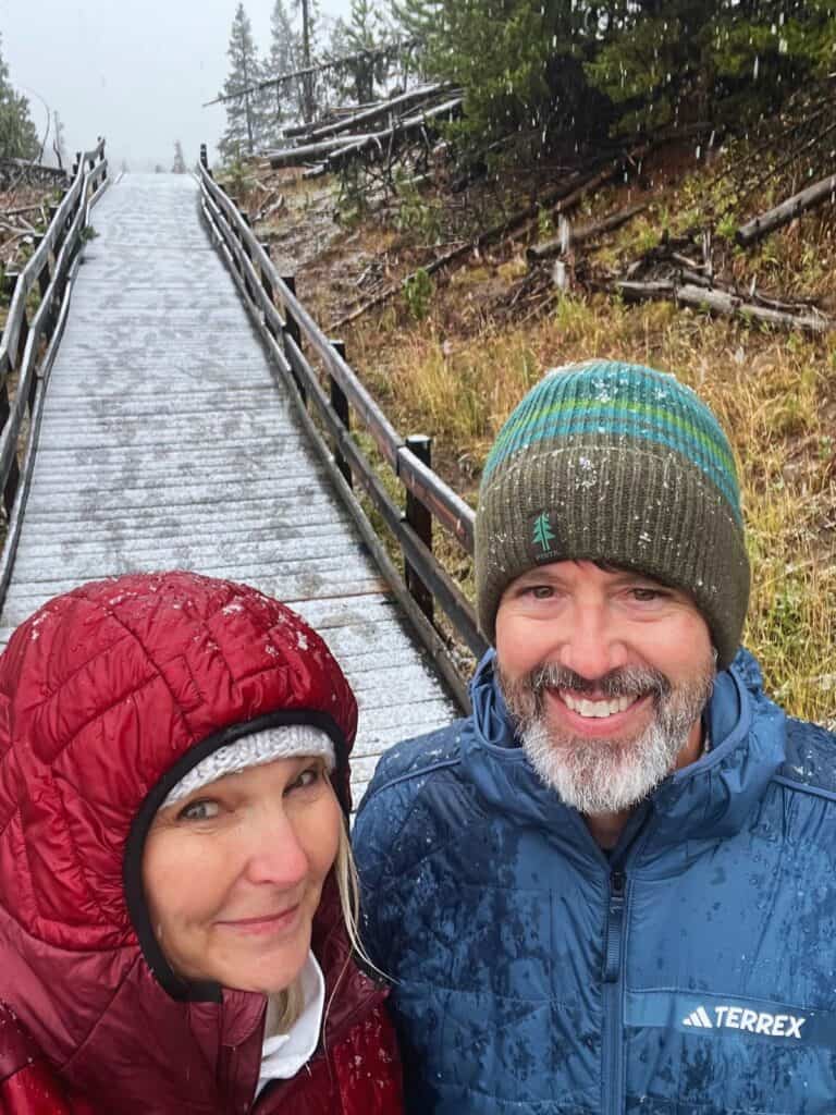 A man and woman pause for a selfie on a boardwalk trail lightly dusted with snow in Yellowstone National Park in early October.