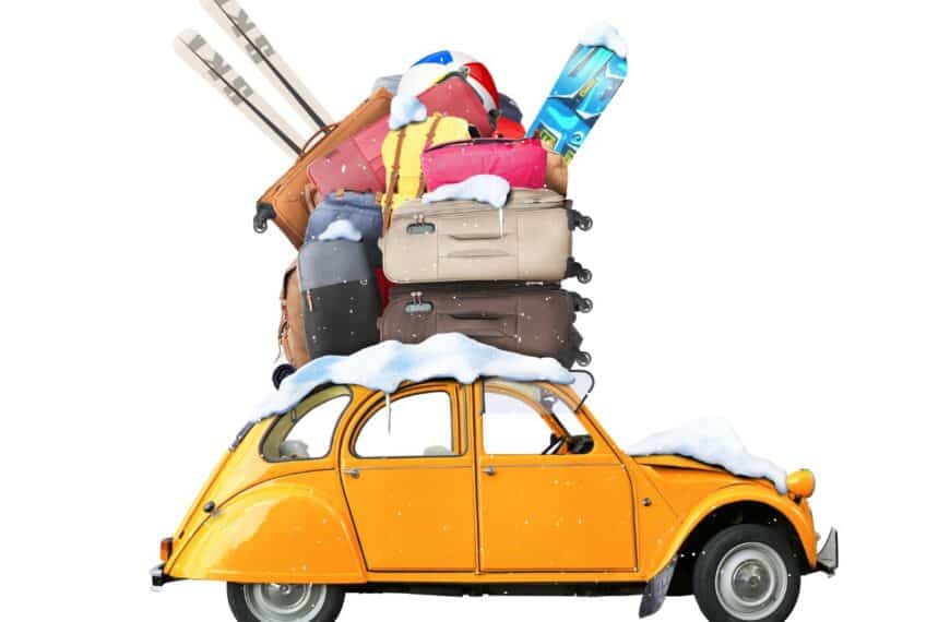 Luggage, winter travel gear, and snow sit on top of a car