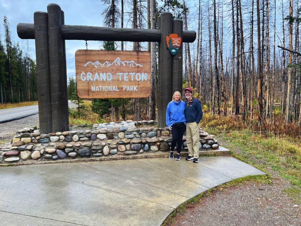 A man and woman stand next to the Grand Teton National Park sign.