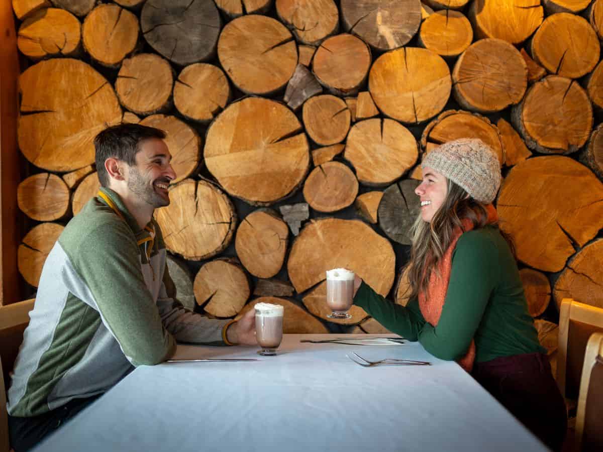 A man and a woman sit at a table, each enjoying a cup of hot cocoa.
