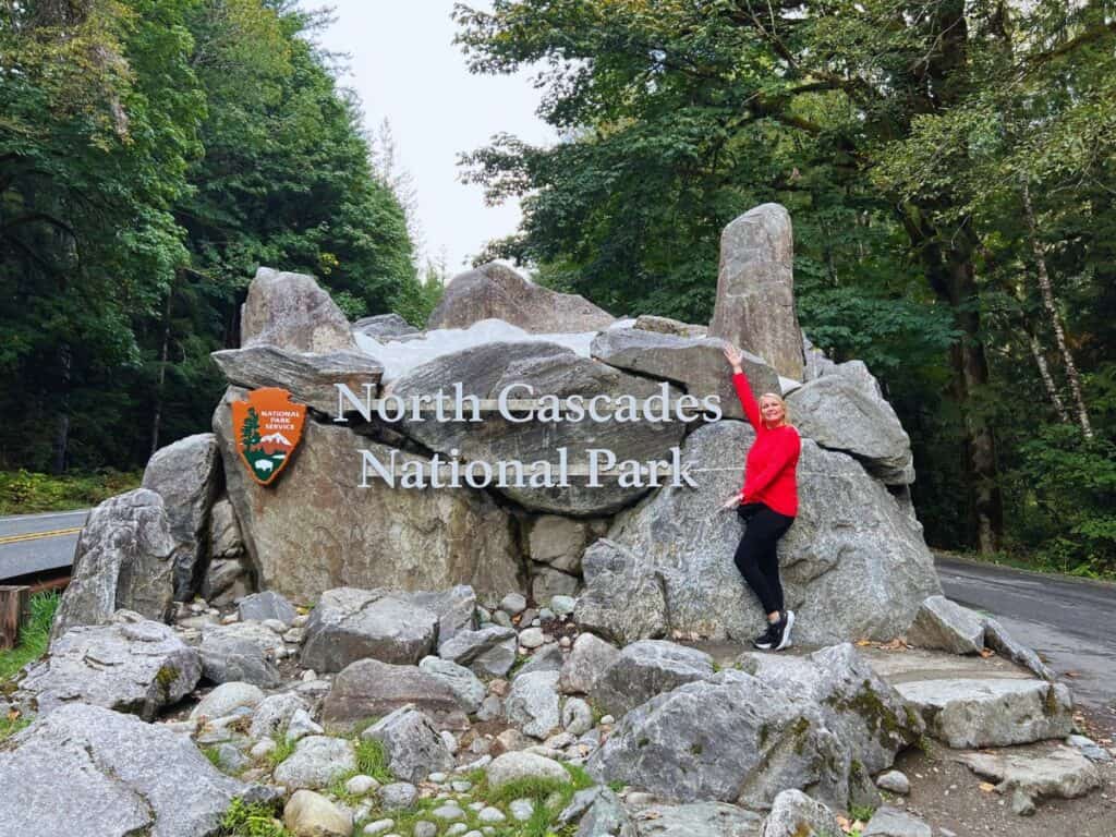 A woman poses for a picture with the North Cascades National Park sign.