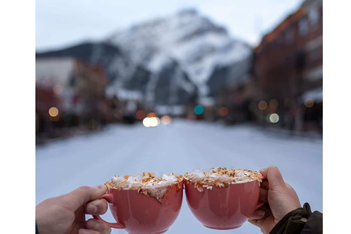 Two people toast with hot chocolate drinks on Banff Avenue during the SnowDays Festival.