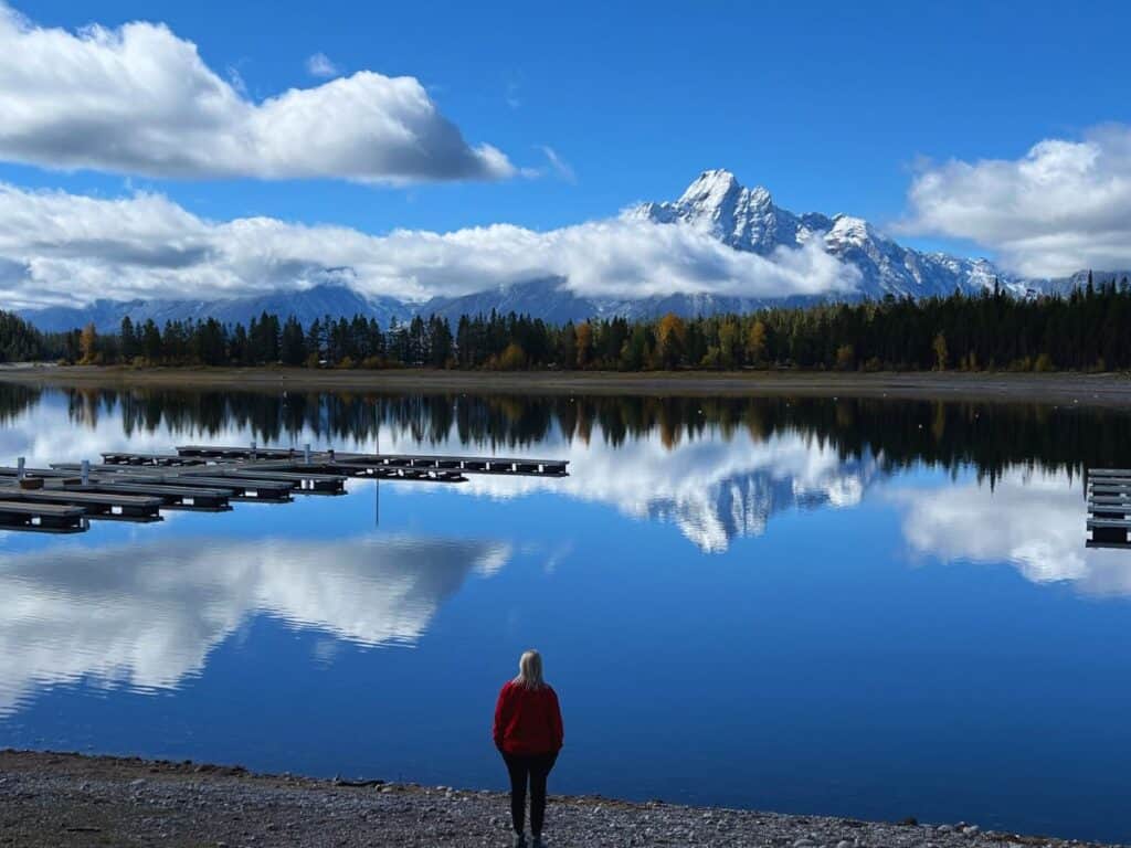 A woman enjoys a view of mountains reflecting in the still water in Grand Teton.