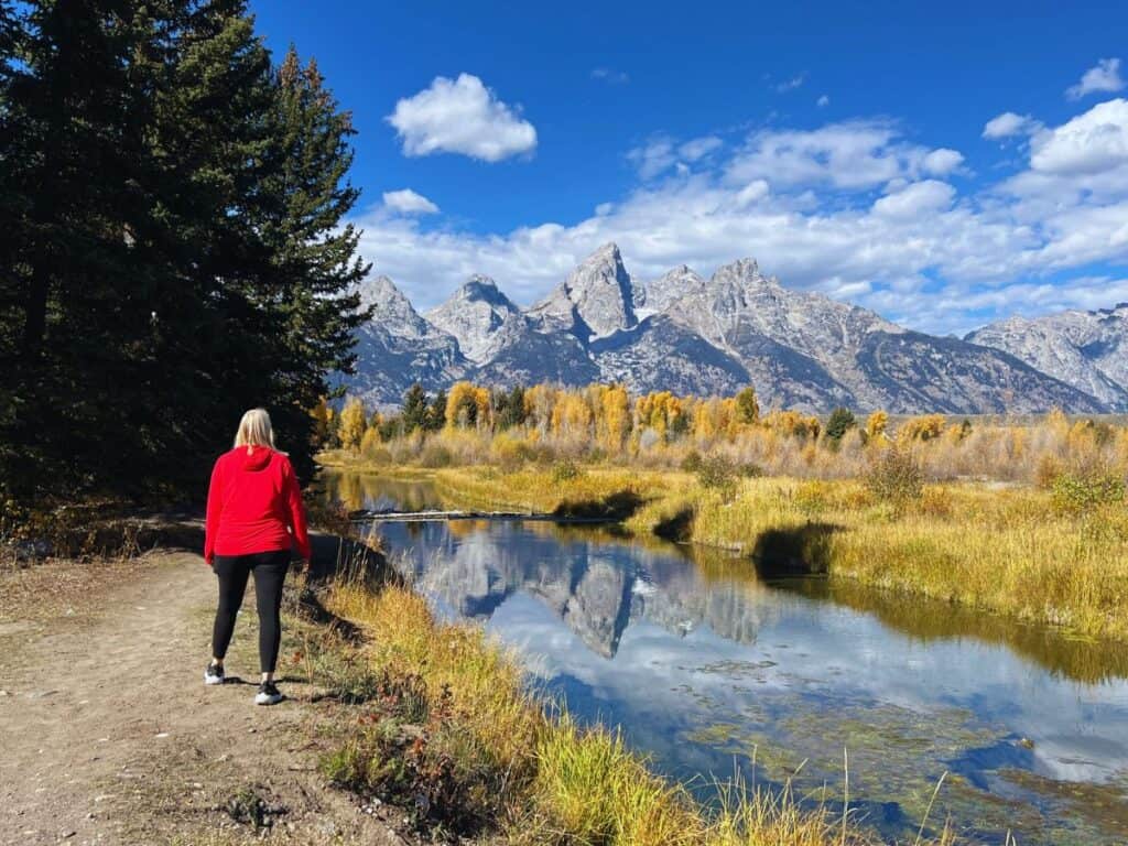 A woman walks along a path where mountain reflections show in the water in Grand Teton National Park, Wyoming.