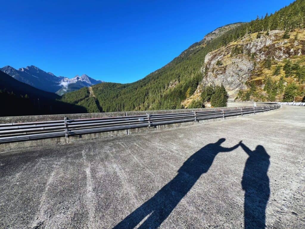 A man and woman give each other a shadow high five on the top of Ross Dam in North Cascades National Park, WA.