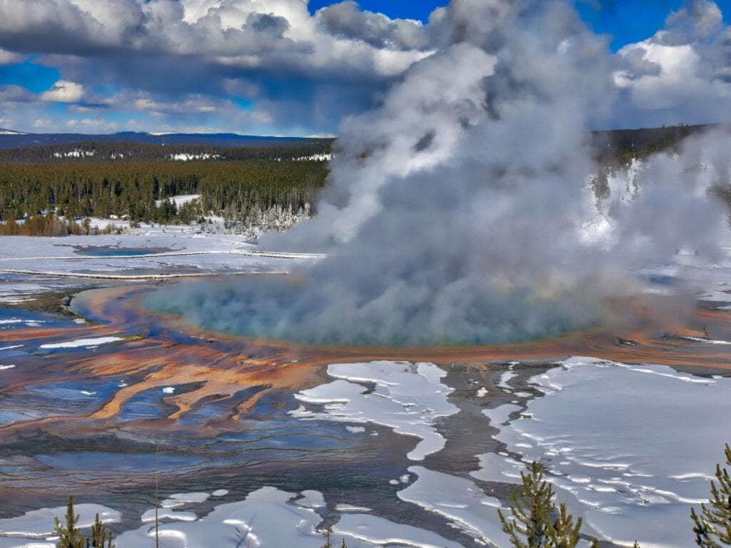 Steam rises from Grand Prismatic with snow surrounding the area