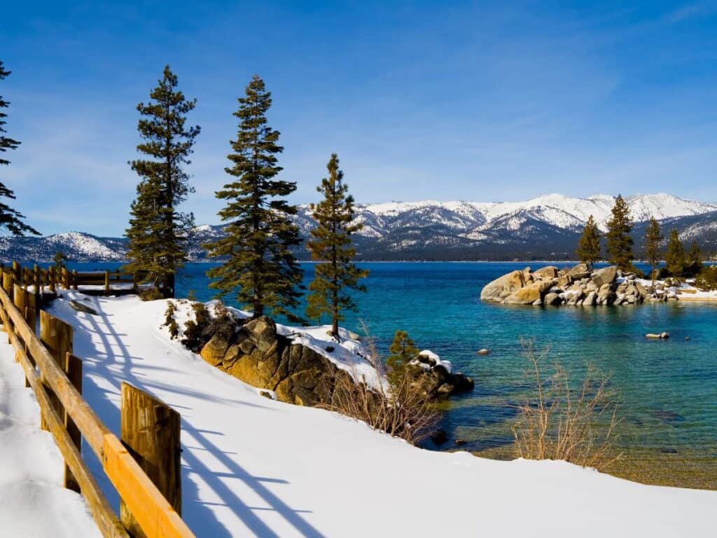 Snowy peaks surround a crystal-clear blue lake with snow on its shores.