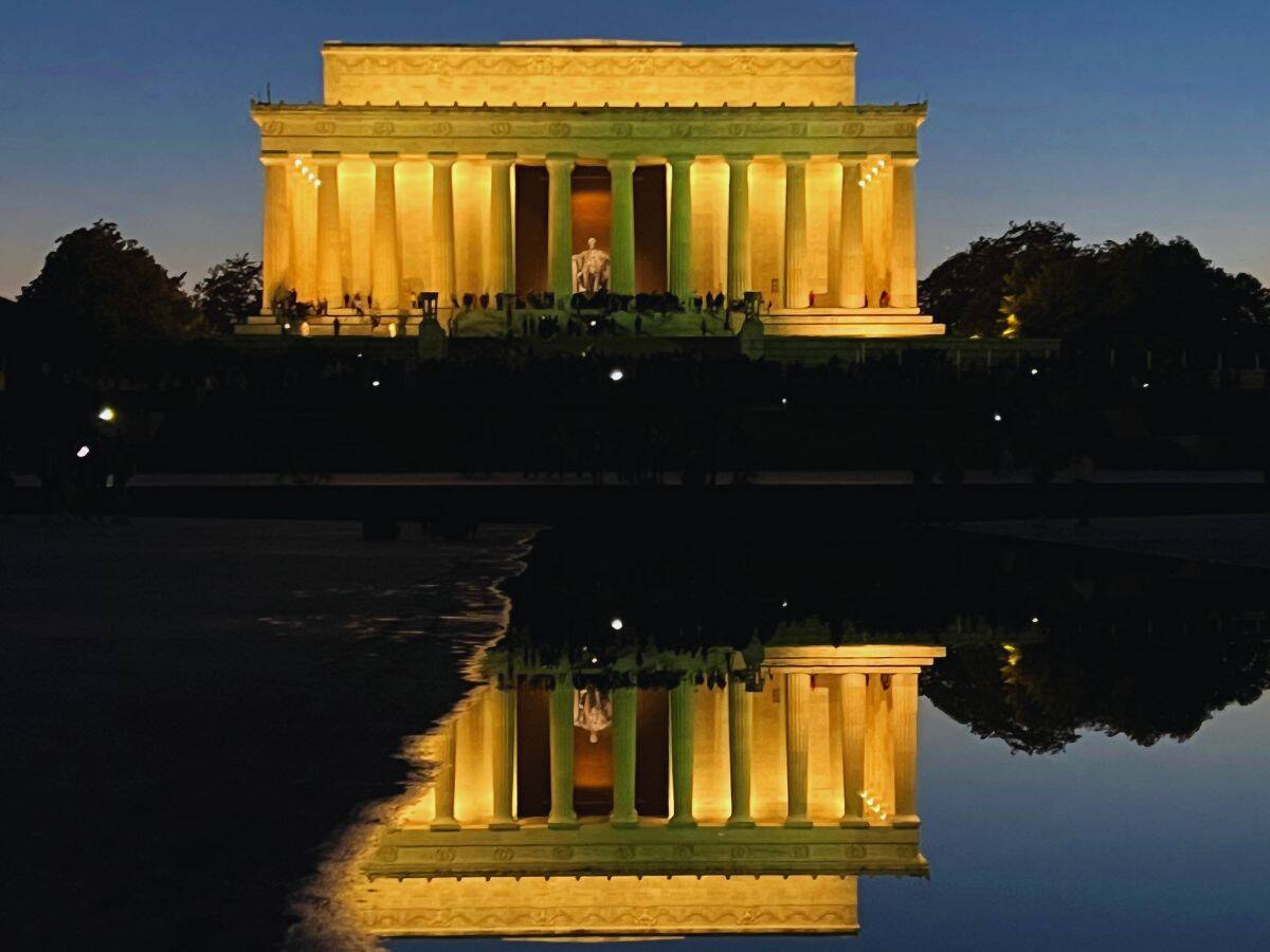 The illuminated Lincoln Memorial reflects in the Lincoln Memorial Reflecting Pool at dusk.